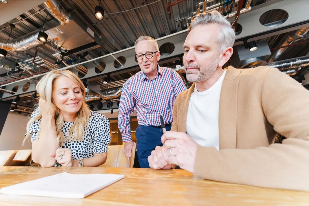 Three business professionals reviewing a document together in a modern, open-plan office setting.