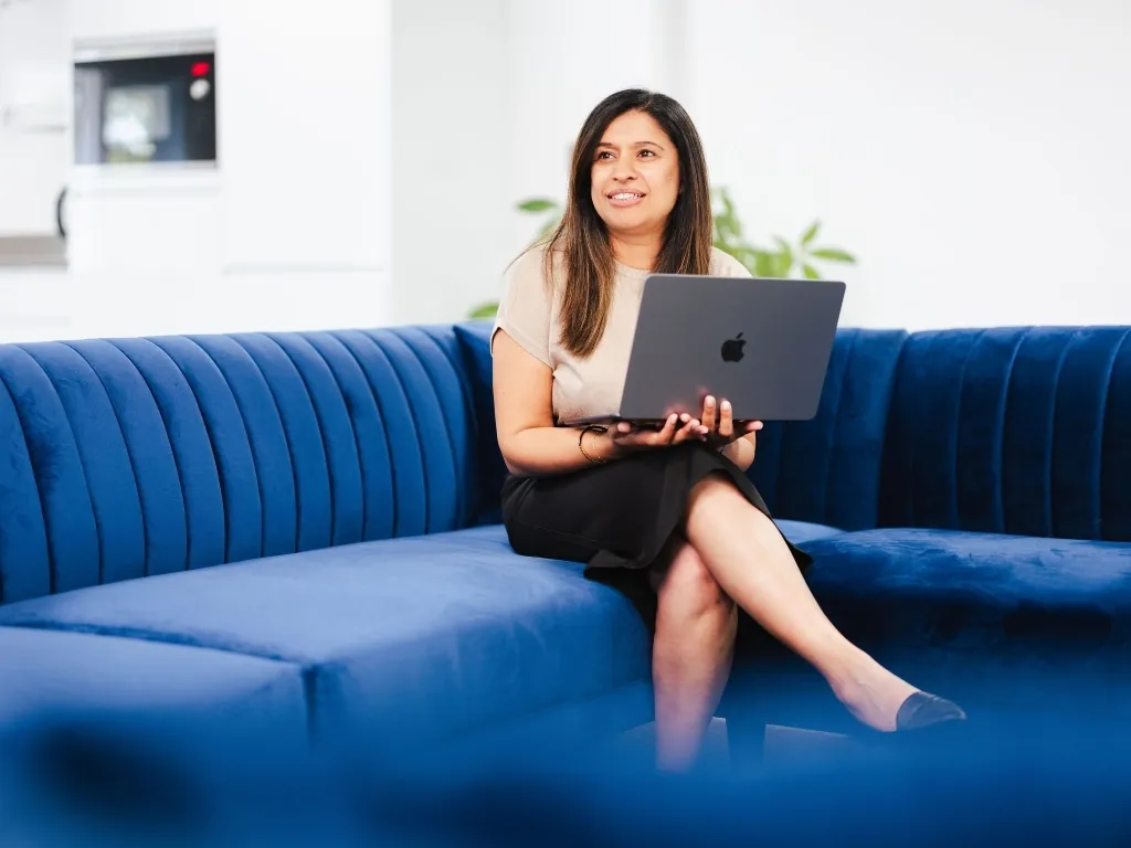 A smiling fractional CFO in a blazer holding a tablet while standing by a window in a bright modern office.