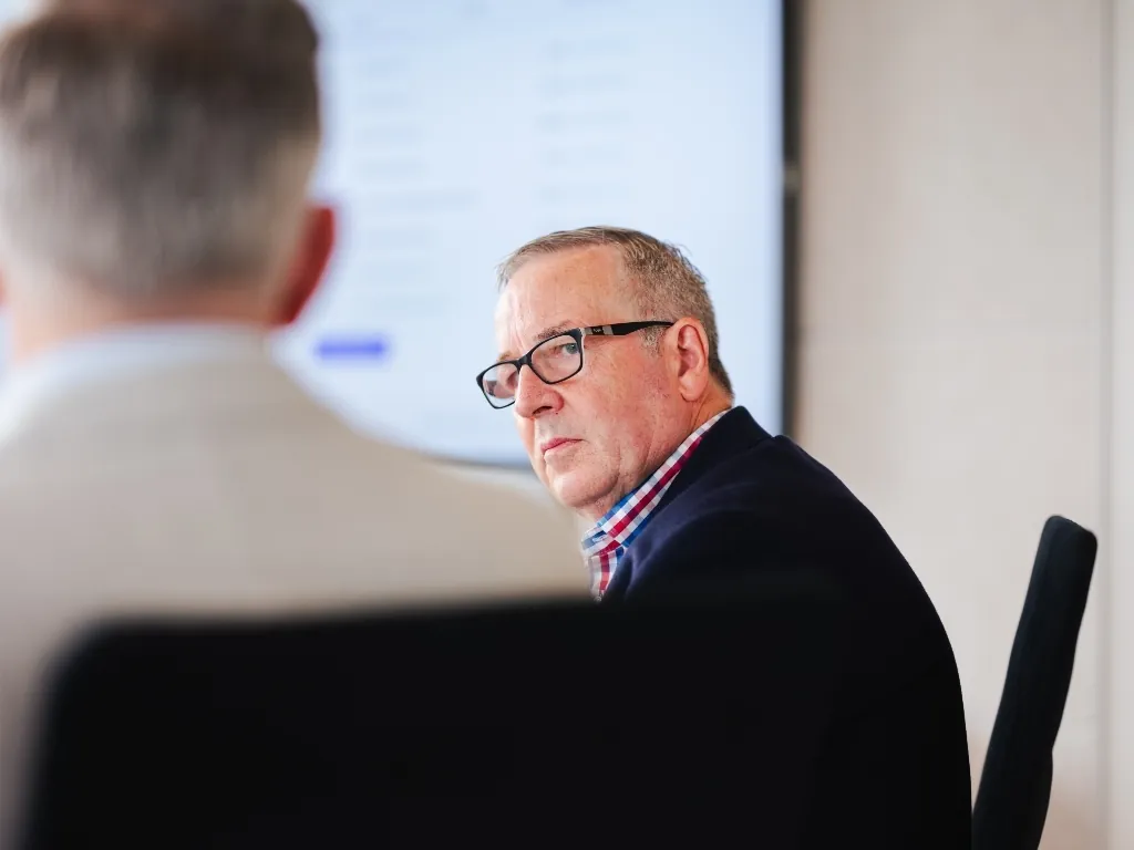 A focused fractional CFO from The CFO Centre wearing glasses and a navy blazer, listening intently during a strategic cash flow consultation with a business owner