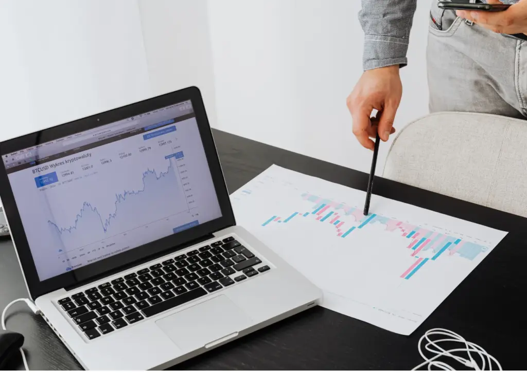 Laptop displaying financial performance charts alongside printed data reports used for market and business analysis